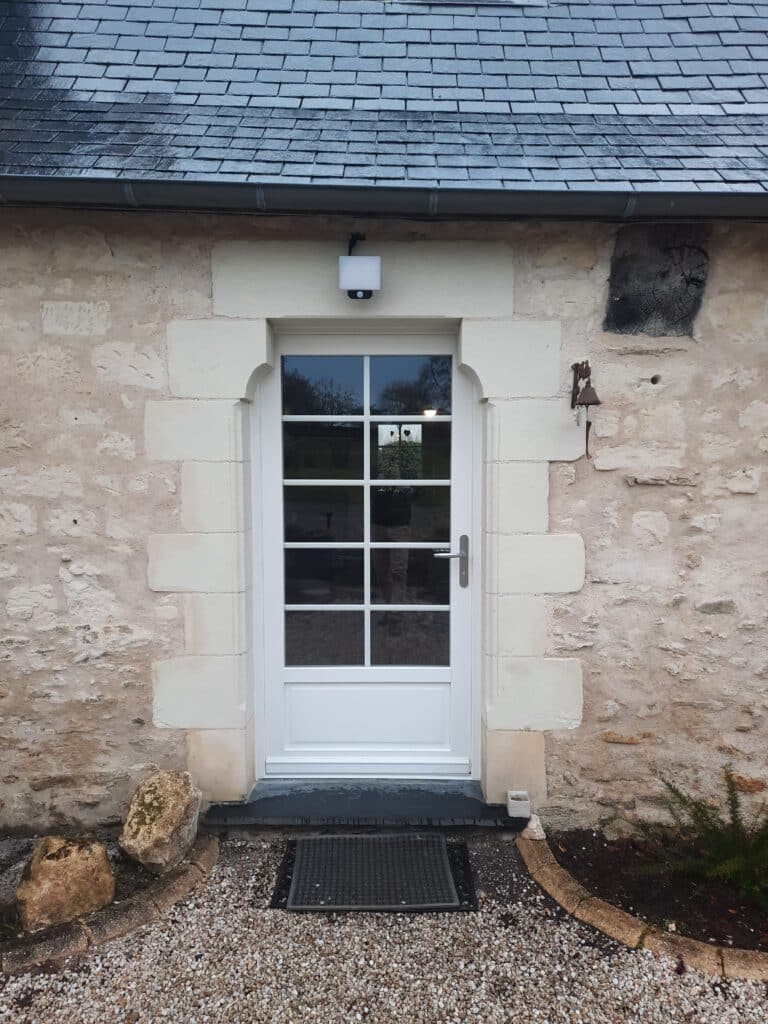 Porte d’entrée PVC blanche installée sur façade en pierre à Mazé, avec seuil bas.